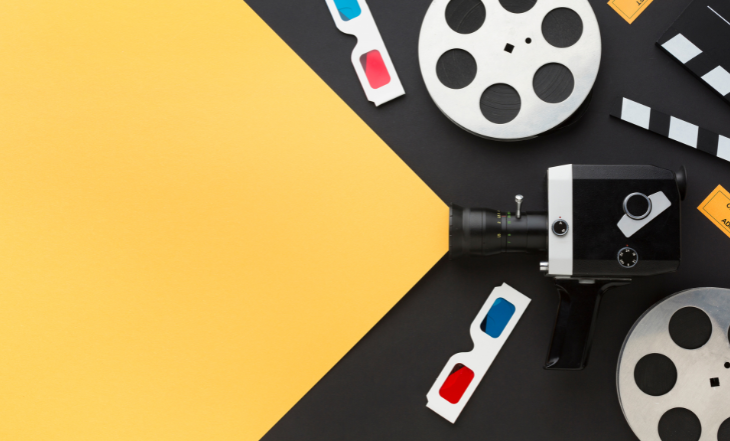 É uma imagem meramente ilustrativa com fundo preto, onde sobre ela aparece rolos de fita de câmeras, óculos de cinema 3D, entre eles parece um câmera, onde da lente sai um facho de luz amarela.